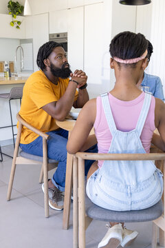African American family eating breakfast in home kitchen around round wooden table with bowl