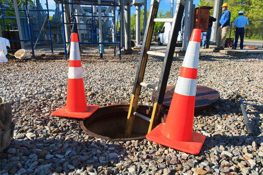 Ladder in manhole and warning cones at high voltage power distribution station