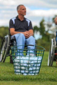 A bucket of golf balls in the foreground and a man in a wheelchair in the background