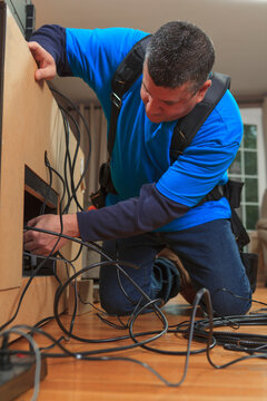 Cable installer working in a home behind the TV
