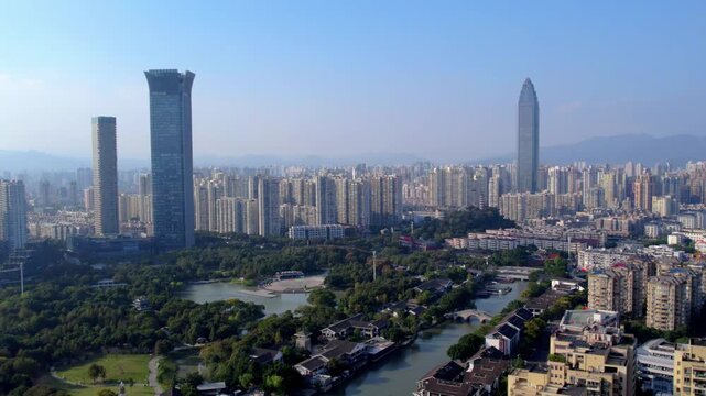 A wide view of a modern urban area featuring skyscrapers, a winding waterway, dense green parks and residential buildings under a clear blue sky.