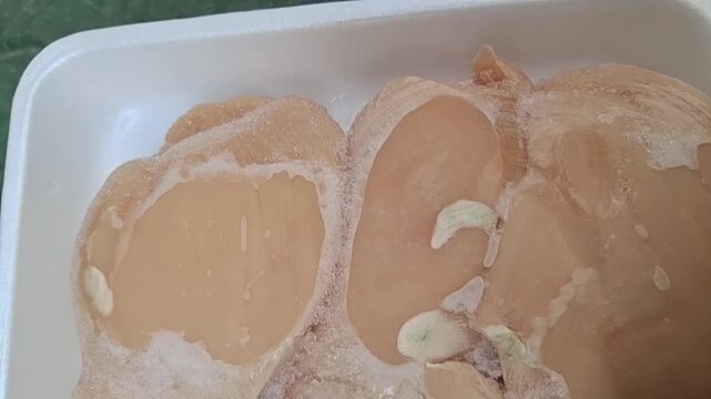 "Close-up of raw chicken breast fillets on a white styrofoam tray. The chicken shows signs of discoloration with visible green patches, indicating spoilage or poor quality, highlighting food safety co