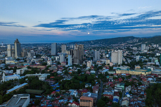 Aerial view of the skyline with skyscrapers and residential neighborhoods under a twilight sky with a full moon and hills in Cebu City, Central Visayas, Philippines.