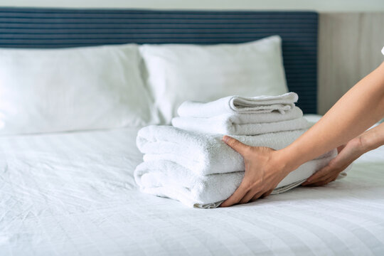 Close up hands of housekeeping  stacked clean towels on the bed in hotel room
