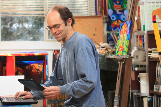 Man with Asperger's working on his tablet and computer in his art studio