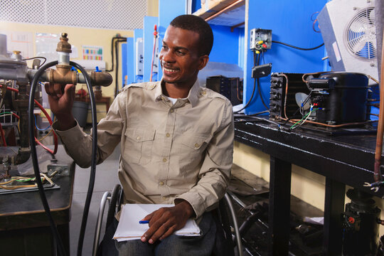 Student in wheelchair examining fuel control valves on furnace in HVAC classroom