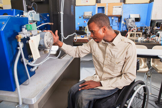 Student in wheelchair studying natural gas injector system on furnace in HVAC classroom
