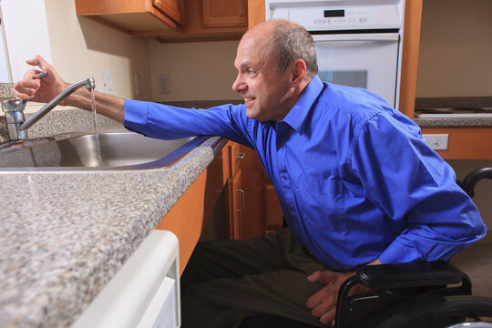 Man with Friedreich's Ataxia and deformed hands using his faucet in the kitchen
