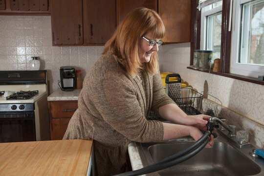 Woman who is legally blind hooking up the portable dishwasher in her kitchen