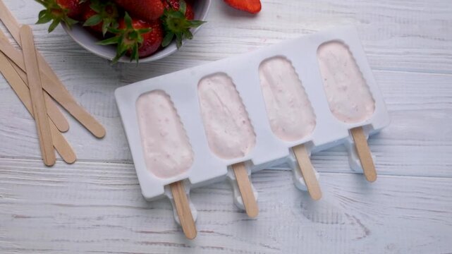 Preparing homemade strawberry popsicles for freezing