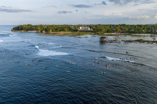 Aerial view of surfers catching waves near the famous Cloud 9 boardwalk and lush tropical coastline of Siargao Island in General Luna, Caraga, Philippines.