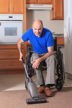 Man with Friedreich's Ataxia and deformed hands vacuuming his house from his wheelchair