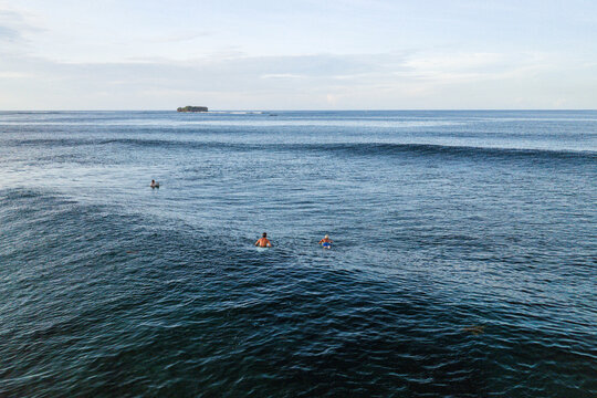 Aerial view of surfers paddling on blue ocean waves near Siargao Island under a clear sky General Luna, Caraga, Philippines.