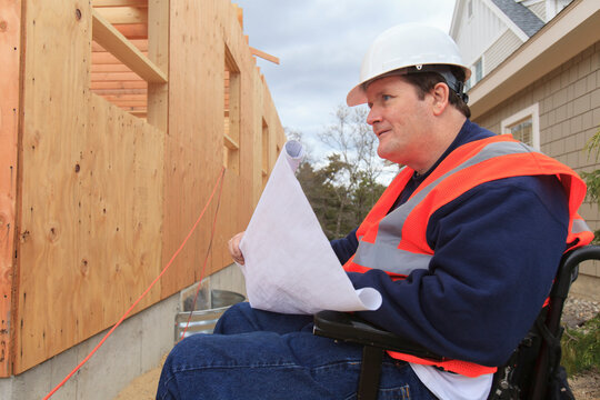 Construction engineer with spinal cord injury holding house plans at construction site