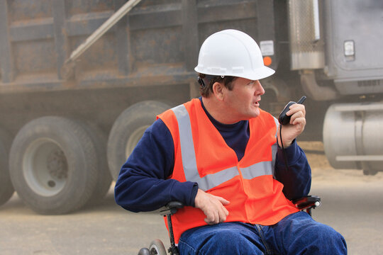 Construction engineer with spinal cord injury talking on radio to dump truck operators