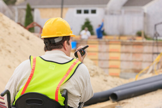 Construction supervisor with Spinal Cord Injury on walkie talkie with foundation and pipes in
