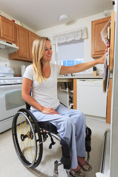 Woman with spinal cord injury in her accessible kitchen looking at notice board