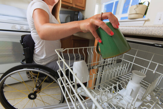 Woman with spinal cord injury in her accessible kitchen putting a cup in dishwasher