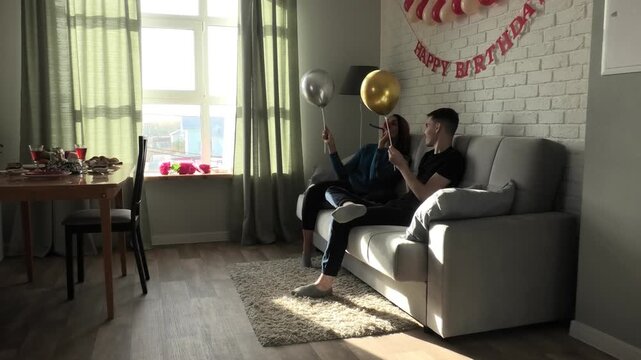 Mother and son blowing party horns and fighting with balloons while sitting on the couch
