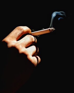 Hand Holding a Lit Cigarette with Smoke on Dark Background
