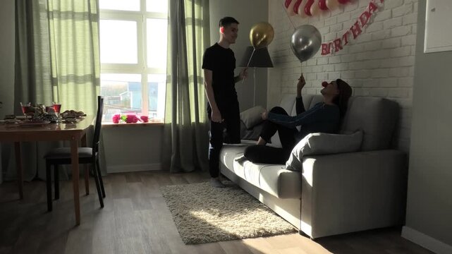 Mother and son blowing party horns and fighting with balloons while sitting on the couch