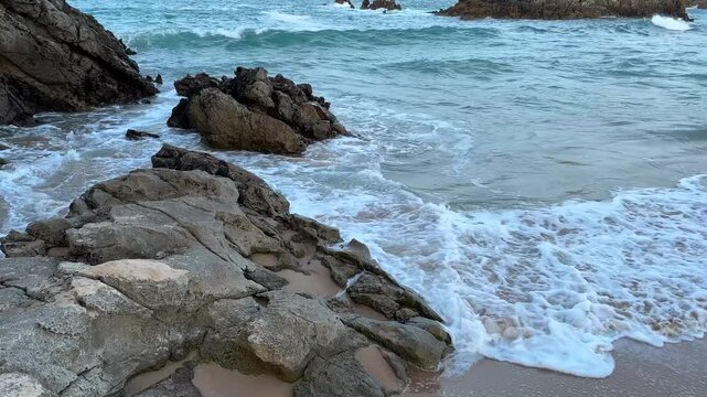 Coastal rocks surrounded by subdued seawater after sunset. Muted evening tones and gentle surf move between the stones in soft post-sunset light.

