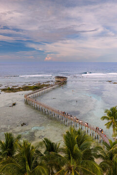 Aerial view of the Cloud 9 boardwalk extending over the turquoise ocean with surfers and palm trees on Siargao Island in General Luna, Caraga, Philippines.