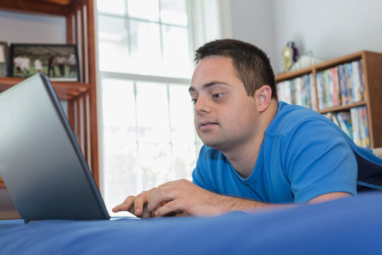 Man with Down Syndrome lying on bed using a laptop