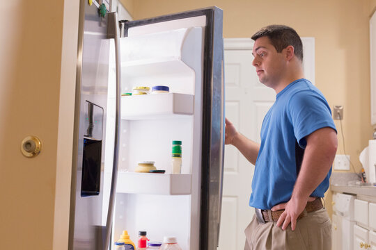 Man with Down Syndrome opening refrigerator in kitchen
