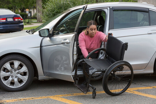 Young woman in the driver's seat of a car prepares her wheelchair for mobility