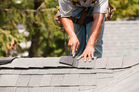 Hispanic carpenter cutting shingles on roof peak
