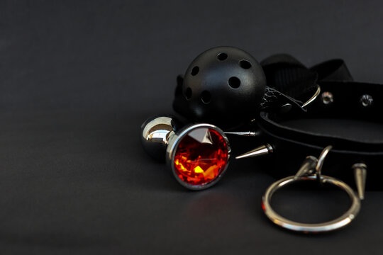 Accessories laid out on a dark surface, showing details of a collar, ball gag, and metal ring used in bondage play