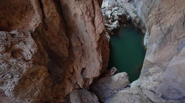 Deep rocky canyon with a clear blue natural pool at a tourist destination, surrounded by steep stone walls and rugged formations, ideal for travel, sightseeing, hiking, geology, and nature tourism con