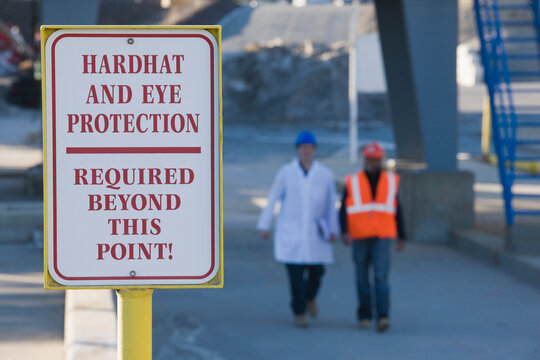 Warning sign saying 'Hardhat and Eye Protection Required Beyond This Point' at an asphalt plant