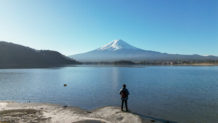 Fototapeta premium Man with backpack standing at Lake Kawaguchiko shore looking at Mount Fuji