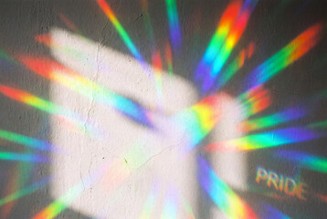 Fototapeta premium Abstract background of vibrant rainbow light refractions on a textured white wall. Colorful prism spectrum beams with the word pride illuminated. LGBTQ equality concept