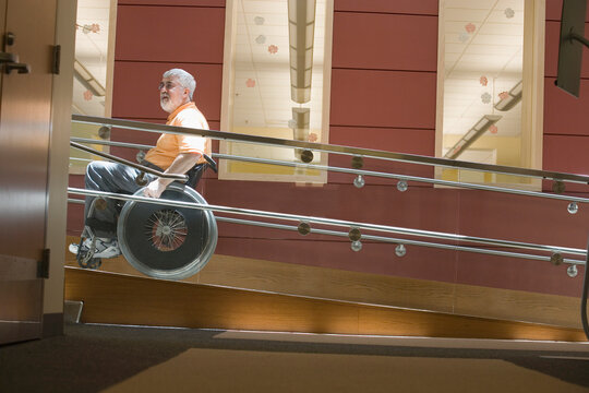 Side profile of a mature man with Muscular Dystrophy sitting in a wheelchair on a wheelchair ramp