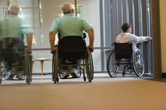 Mature man with Muscular Dystrophy and a young woman sitting in wheelchairs in a library