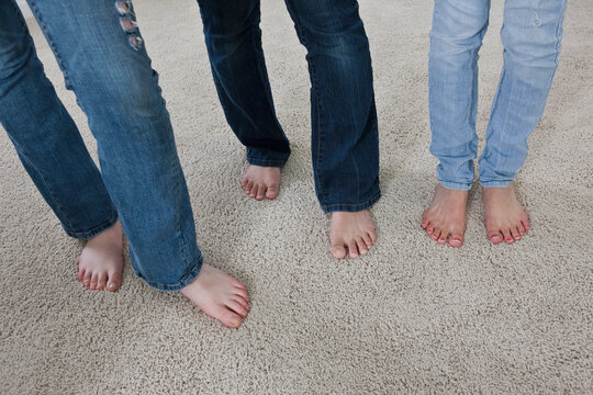 Three sets of legs wearing denim jeans and bare feet standing on carpet