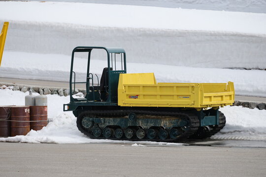 A small tracked dumper parks near the snow wall.