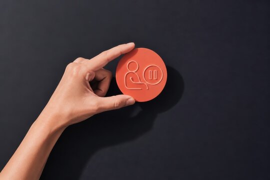 Hand holding orange token with user and pause icon on dark background
