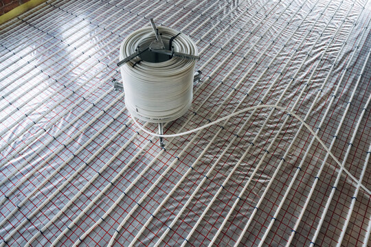 Heating system installation with white tubing coiled on the floor, laid out in a grid pattern on a construction site for underfloor heating system