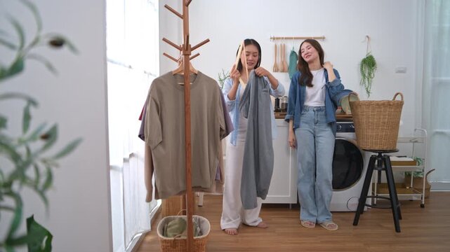 Two young Asian women organizing freshly washed clothes and preparing garments for hanging on a clothing rack