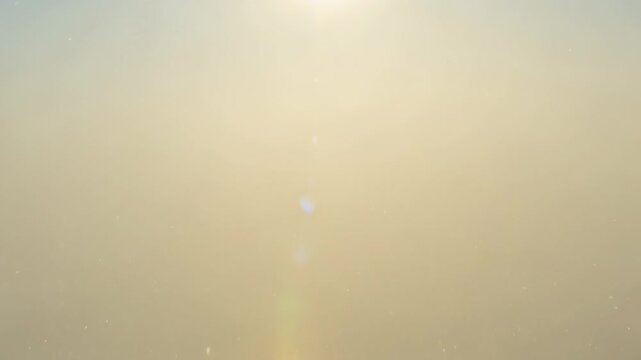 Glinting sun creating vertical lens flare and sending dust particles drifting in hazy sky