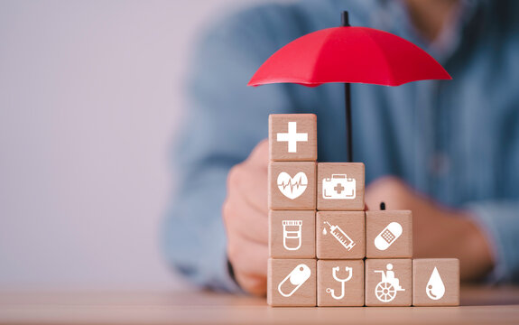 Healthcare insurance protection concept with red umbrella covering wooden blocks icons of medical care, medicine, disability, blood, vaccine and emergency support for health security.