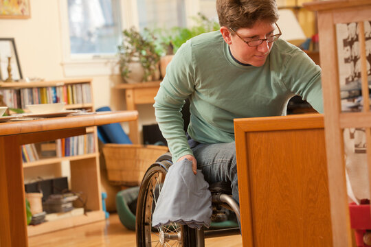 Woman with multiple sclerosis in a wheelchair getting table settings from accessible cupboard