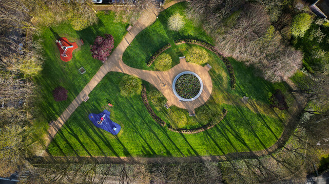 Aerial view of a public park with a circular flower bed, winding paths, and a children's playground among green lawns and trees in Morlaix, Brittany, France.