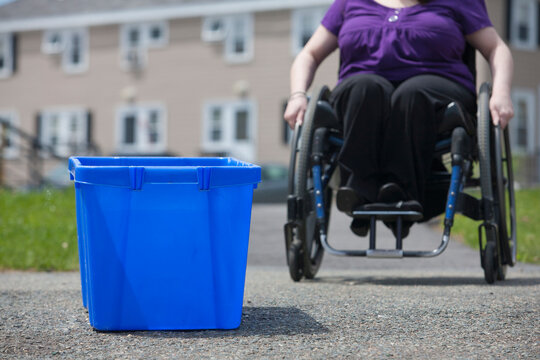 Woman with Spina Bifida in a wheelchair coming to pick up a recycling bin at the street