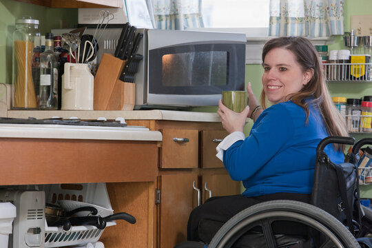 Woman with Spina Bifida in a wheelchair using her microwave in the accessible kitchen