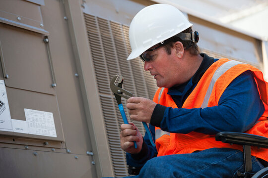 Facilities engineer in a wheelchair opening inspection plate of commercial air conditioning system